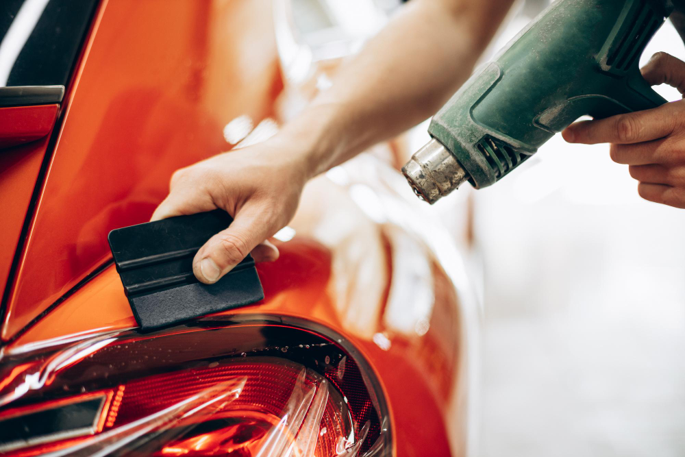 A worker installs clear PPF using a heat gun in a red car