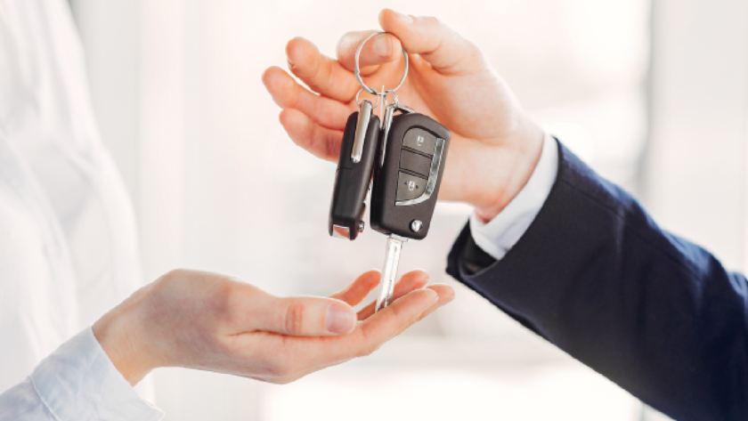 Close-up of a person handing over car keys to another person, symbolising car sale or resale transaction.