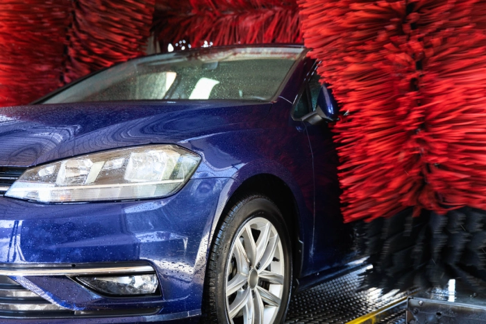 A blue coloured car passes through an automatic brush car washer