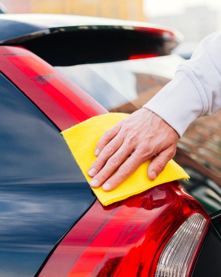 Close shot of a car’s window and edge being cleaned with a yellow wipe
