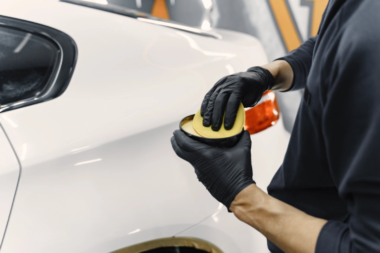 A worker prepares to apply wax from a tin on a car inside a garage