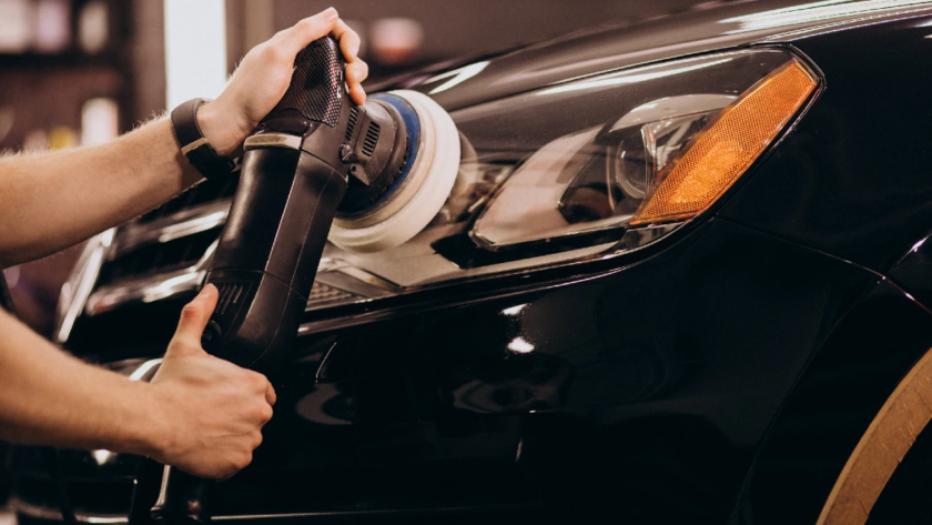Professional detailer performing paint correction on a black car using a machine polisher to restore gloss and prepare the surface for PPF coating.