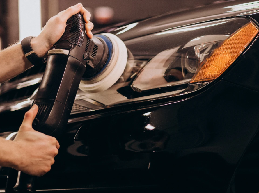 Professional detailer performing paint correction on a black car using a machine polisher to restore gloss and prepare the surface for PPF coating.