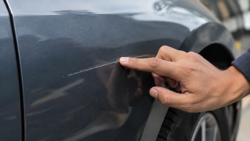 Hand testing the depth of a car paint scratch